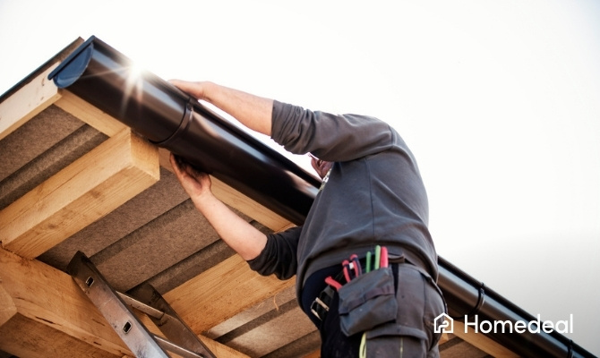 Dakgoot vervangen door een vakman die een nieuwe hemelwaterafvoer aan de dakrand monteert van een woning of overkapping.