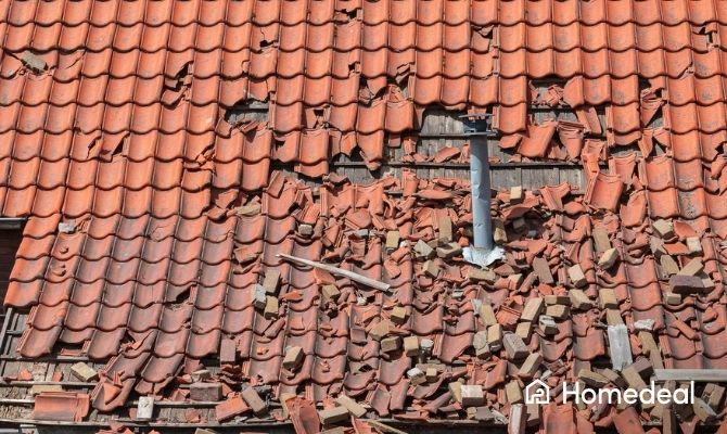 Dakreparatie van een zwaar beschadigd pannendak met gebroken dakpannen en puin op het dak na storm- of valschade. Het dak is toe aan een spoedreparatie.