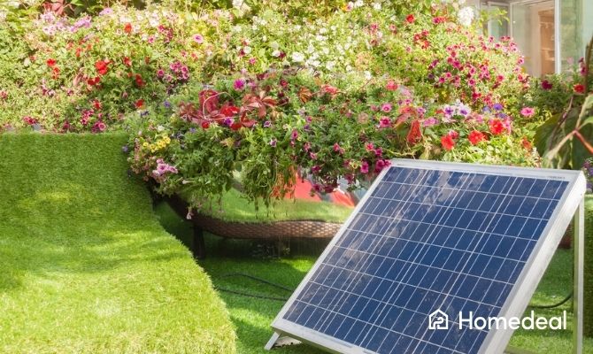 Losstaand zonnepaneel geplaatst in een zonnige tuin met kunstgras en een overvloed aan kleurrijke bloemen op de achtergrond.