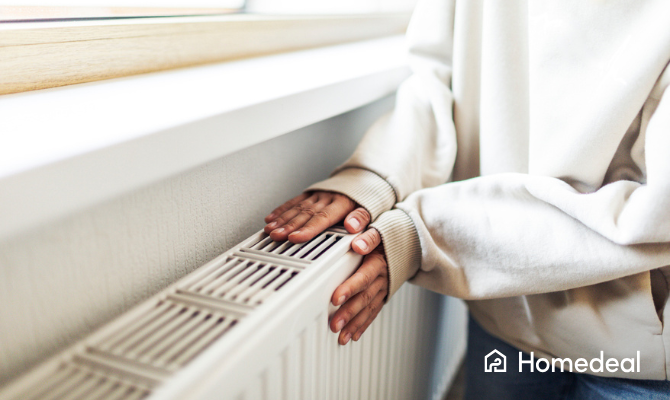 Vrouw in dikke sweater houd haar beide handen tegen een radiator