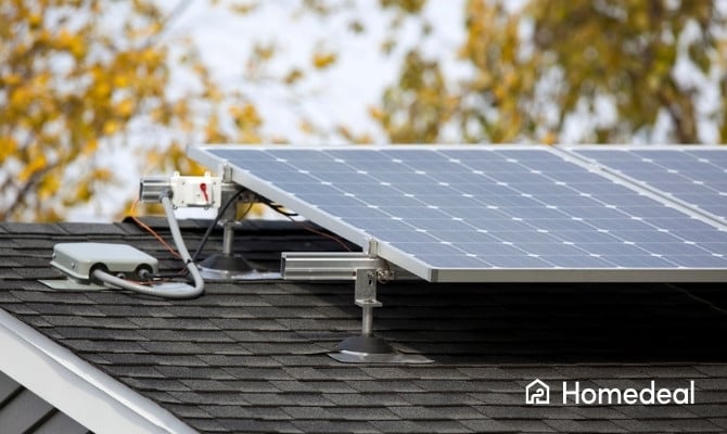 Close-up van een zonnepaneel op een schuin dak met dakshingles, uitgerust met een power optimizer voor optimale energieopbrengst, met herfstbladeren op de achtergrond.