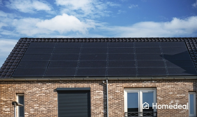 Woning met zwarte zonnepanelen op schuin dak onder blauwe lucht.