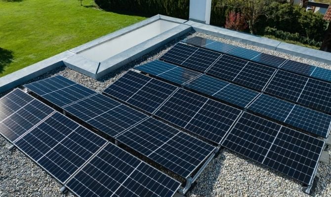 Zonnepanelen geïnstalleerd op plat dak van woning met grindbedekking.