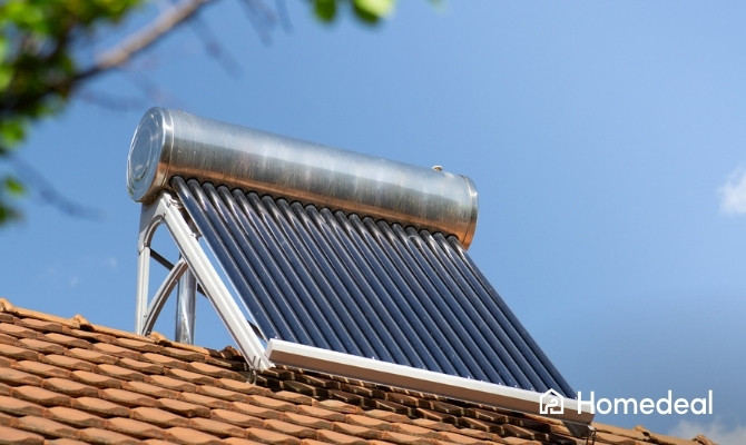 Close-up van een vacuümbuis zonnecollector op een rood pannendak, gebruikt voor het opwekken van warm water met zonne-energie, tegen een heldere blauwe lucht.