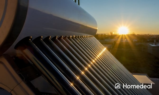 Close-up van een zonneboiler met vacuümbuizen die zonlicht opvangen tijdens zonsondergang, met een stadse horizon op de achtergrond.