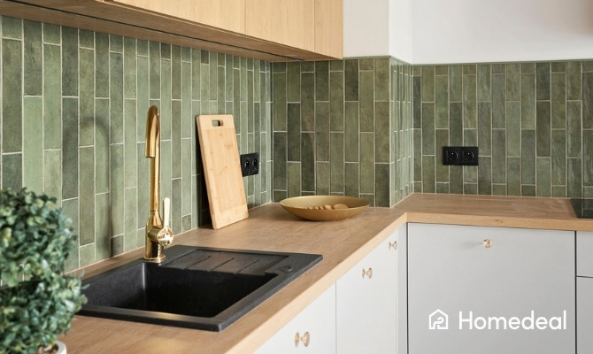 Stijlvolle witte keuken met houten werkblad, groene wandtegels, zwarte spoelbak en goudkleurige kraan.