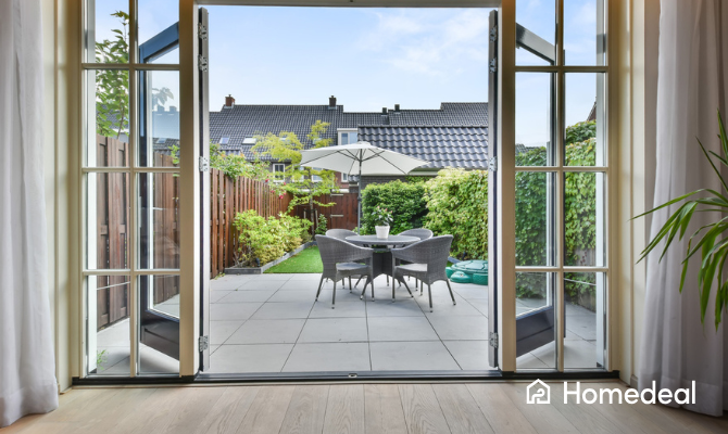 Je ziet vanuit een huiskamer openslaande deuren naar een strak terras in een nieuw aangelegde tuin