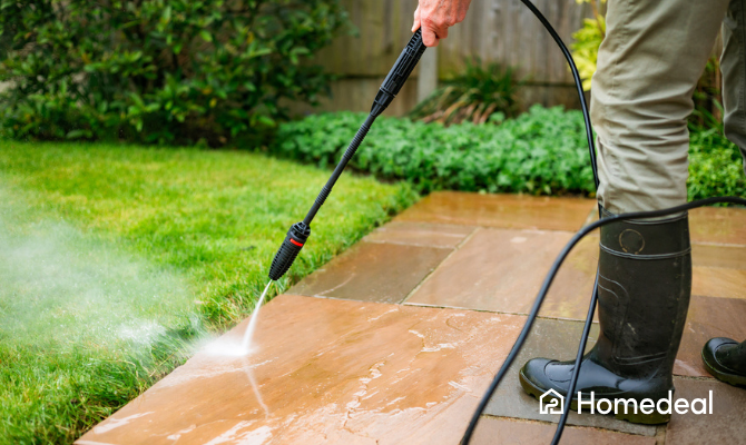 Man met laarzen reinigt stenen terras met hogedrukspuit