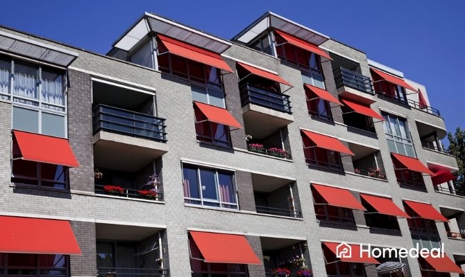 Appartementencomplex met rode uitvalschermen als buitenzonwering boven ramen en balkons.