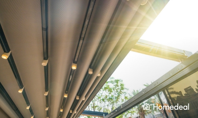 Close-up van een moderne veranda met uitschuifbare stoffen zonwering in beige/taupe kleur, voorzien van ingebouwde LED-spotjes langs de aluminium railgeleiders. 