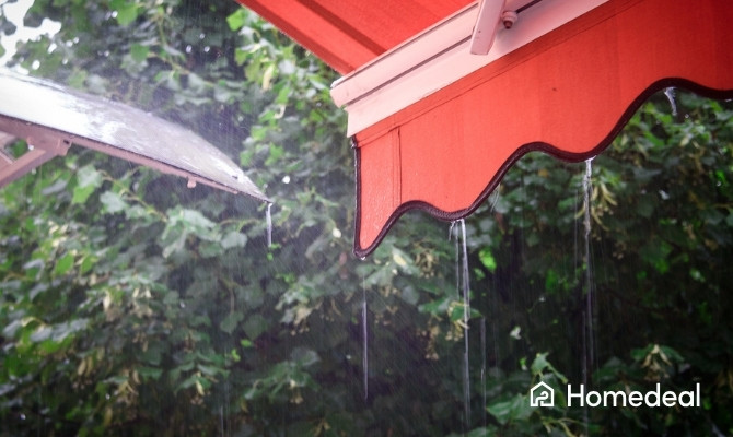 Rood waterdicht zonnescherm met regendruppels tijdens een stevige regenbui in een groene tuin.