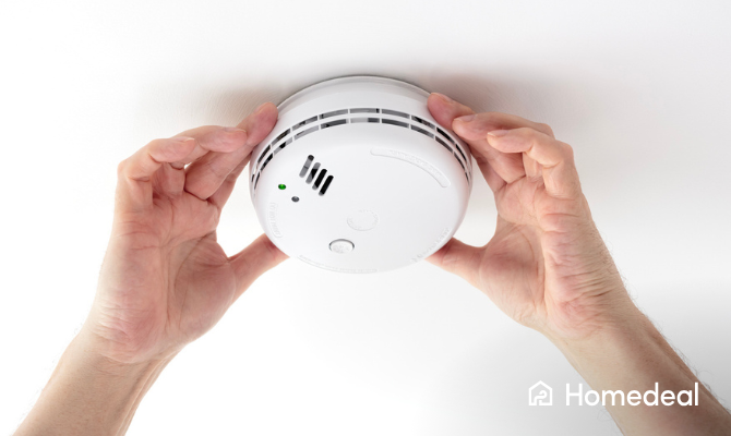 Close up van twee handen die een brandmelder plaatsen op een plafond