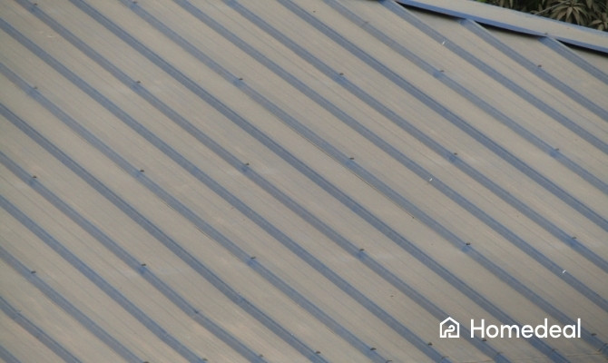 Close-up van metalen dakplaten op een schuin dak met geprofileerde banen en zichtbare bevestigingen. Deze duurzame dakplaten worden veel toegepast op woningen, schuren en bedrijfspanden.