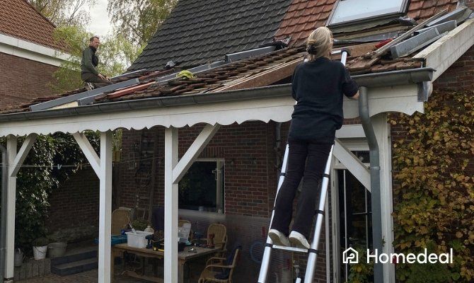 Bewoner kijkt vanaf een ladder toe terwijl een dakdekker de dakbedekking van de overkapping vervangt.