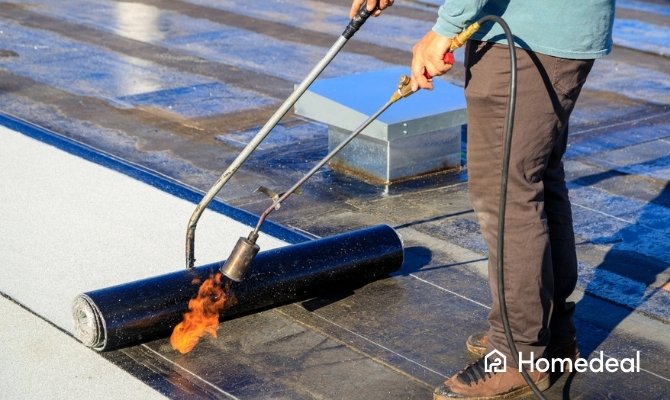 Dakdekker is dakleer aan het branden op een plat dak met een gasbrander om de bitumen dakbedekking waterdicht te bevestigen.