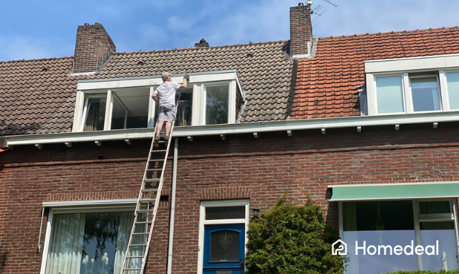 Grote dakkapel wordt opgeschuurd door een man op een ladder