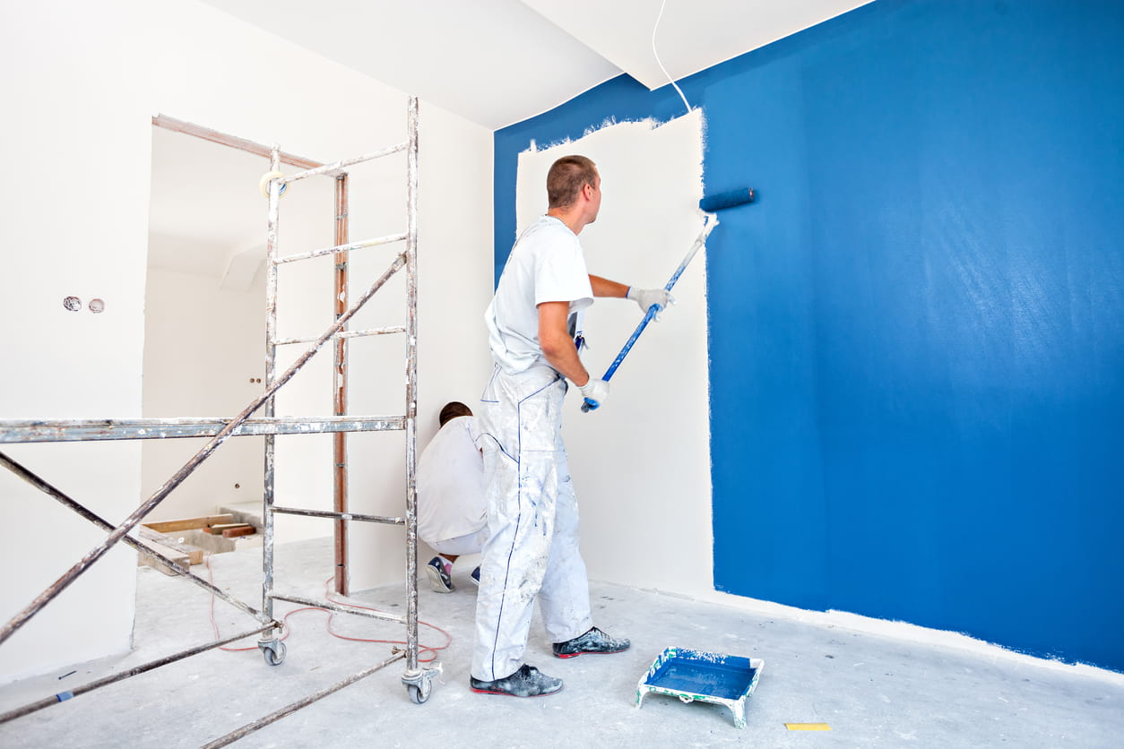 schilder die gehurkt met kwast in de hand de muur verft