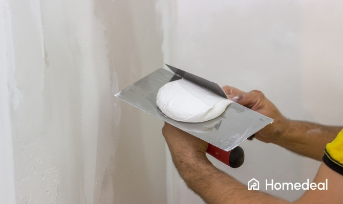 Close-up van iemand die verse pleister op een spaan schept tijdens het muur stucen en voorbereiden van glad stucwerk.
