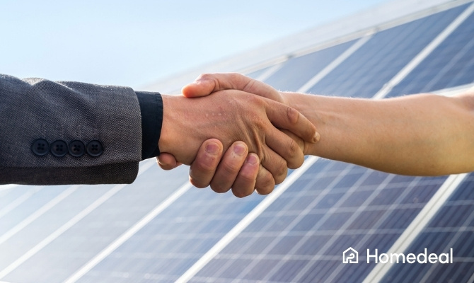 Close-up van twee mensen die elkaar de hand schudden voor een overeenkomst over het leasen van zonnepanelen, met zonnepanelen in de achtergrond.