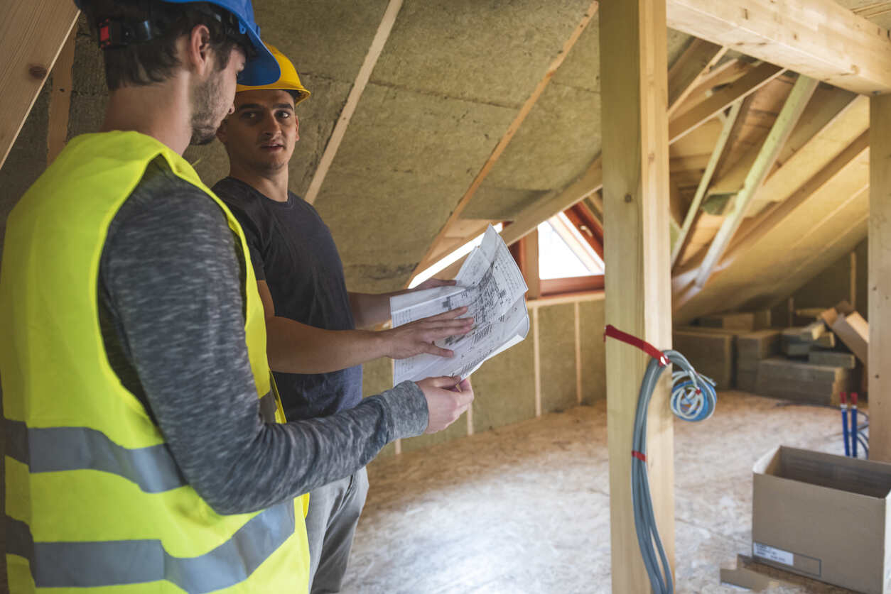 Huiseigenaar en aannemer staan op een zolder in aanbouw en bespreken een bouwtekening. 