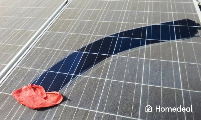 Close-up van zonnepanelen waarbij een rode doek een schoongeveegd deel achterlaat, duidelijk contrasterend met het stoffige oppervlak.