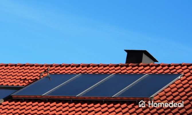 Close-up van hybride zonnepanelen op een rood pannendak, ontworpen om zowel elektriciteit als warmte op te wekken, met op de achtergrond een heldere blauwe lucht.