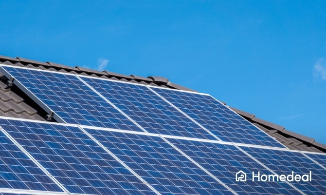 Close-up van polykristallijne zonnepanelen op een schuin dak met donkere dakpannen onder een heldere blauwe lucht.