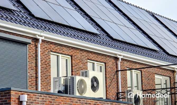 Close-up van een rijtjeshuis met glanzende PVT-panelen op het dak en meerdere lucht/lucht-warmtepompen aan de gevel voor duurzame verwarming en koeling.