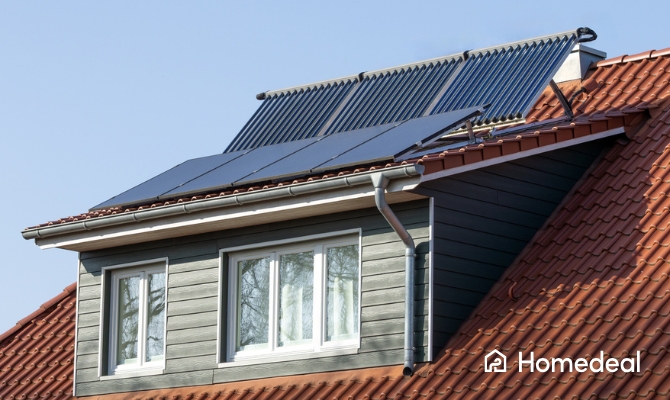Woning met rode dakpannen en een dakkapel, waarop zwarte zonnepanelen zijn geplaatst; boven de dakkapel bevinden zich zonnecollectoren voor warmwateropwekking.