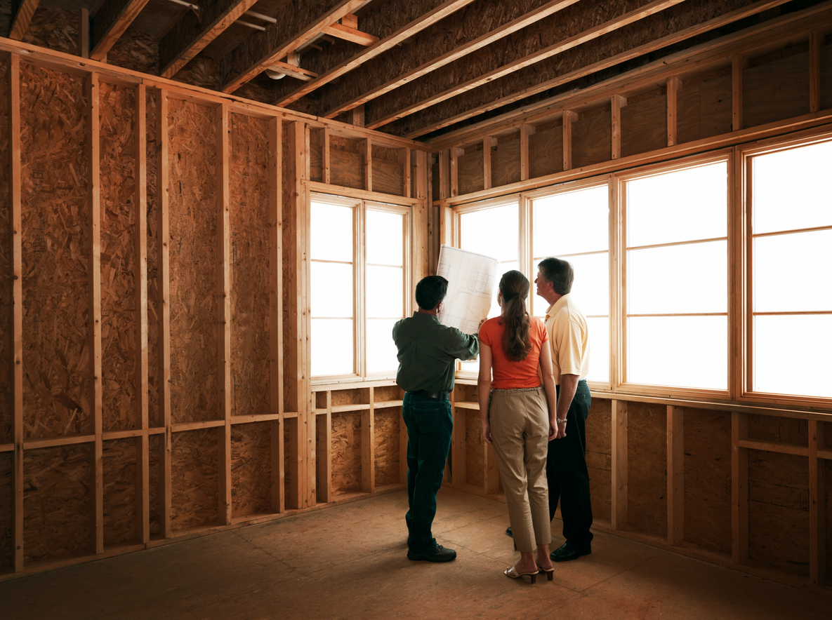 Huiseigenaren en vakspecialist staan in een houten uitbouw die wordt gebouwd en houden een bouwtekening in de lucht