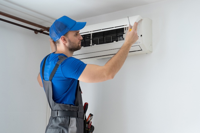 Mannelijke airco installateur in een blauw overal installeert of repareert een airco aan de muur