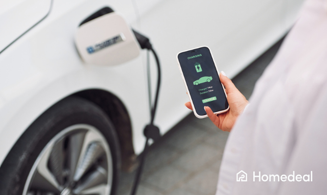 Vrouw houdt telefoon met app van slimme laadpaal vast op de achtergrond zie je de elektrische auto laden