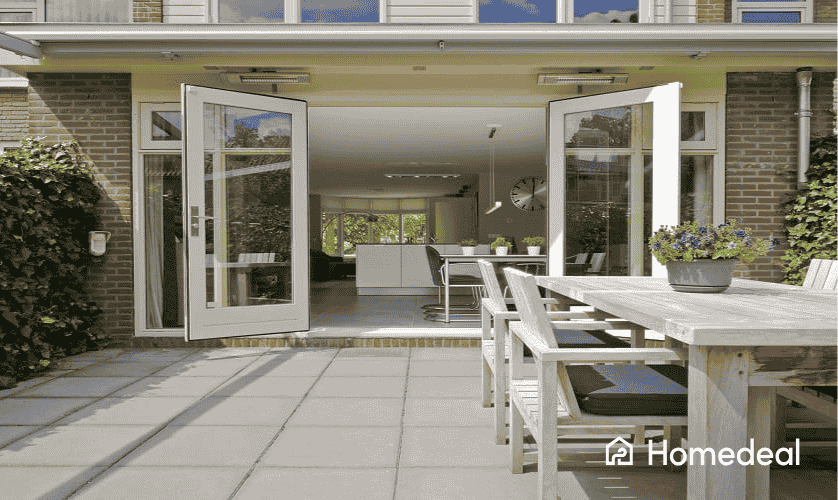 Moderne aanbouw met openslaande deuren naar een betegeld terras met houten tuinset