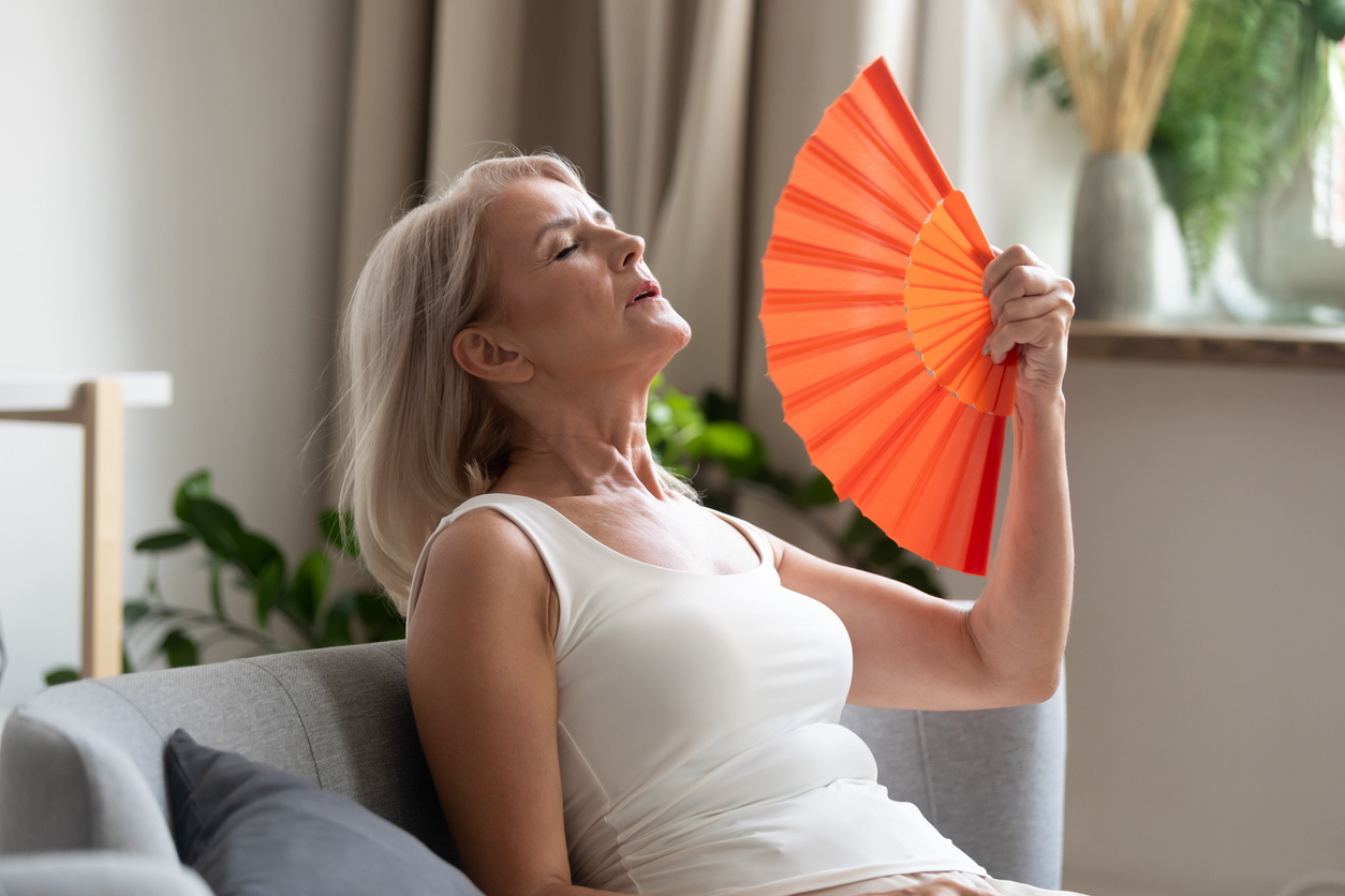 Oudere vrouw met waaier wappert koele wind in haar gezicht vanwege de hitte
