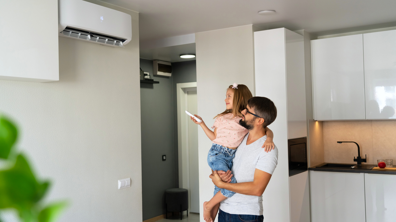 Vader houdt dochter vast, dochter heeft afstandsbediening van airco vast en richt deze op de airco aan de muur in het appartement
