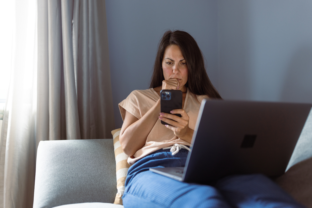 Slachtoffer van fraude. Vrouw zit op bank met laptop en telefoon en kijkt angstig en gestrest.